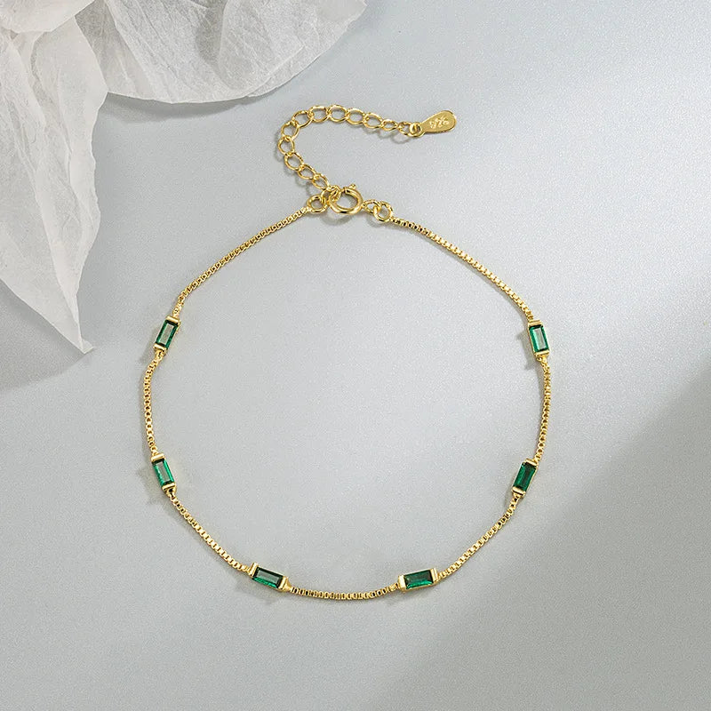 A delicate gold bracelet with small emerald gemstones.