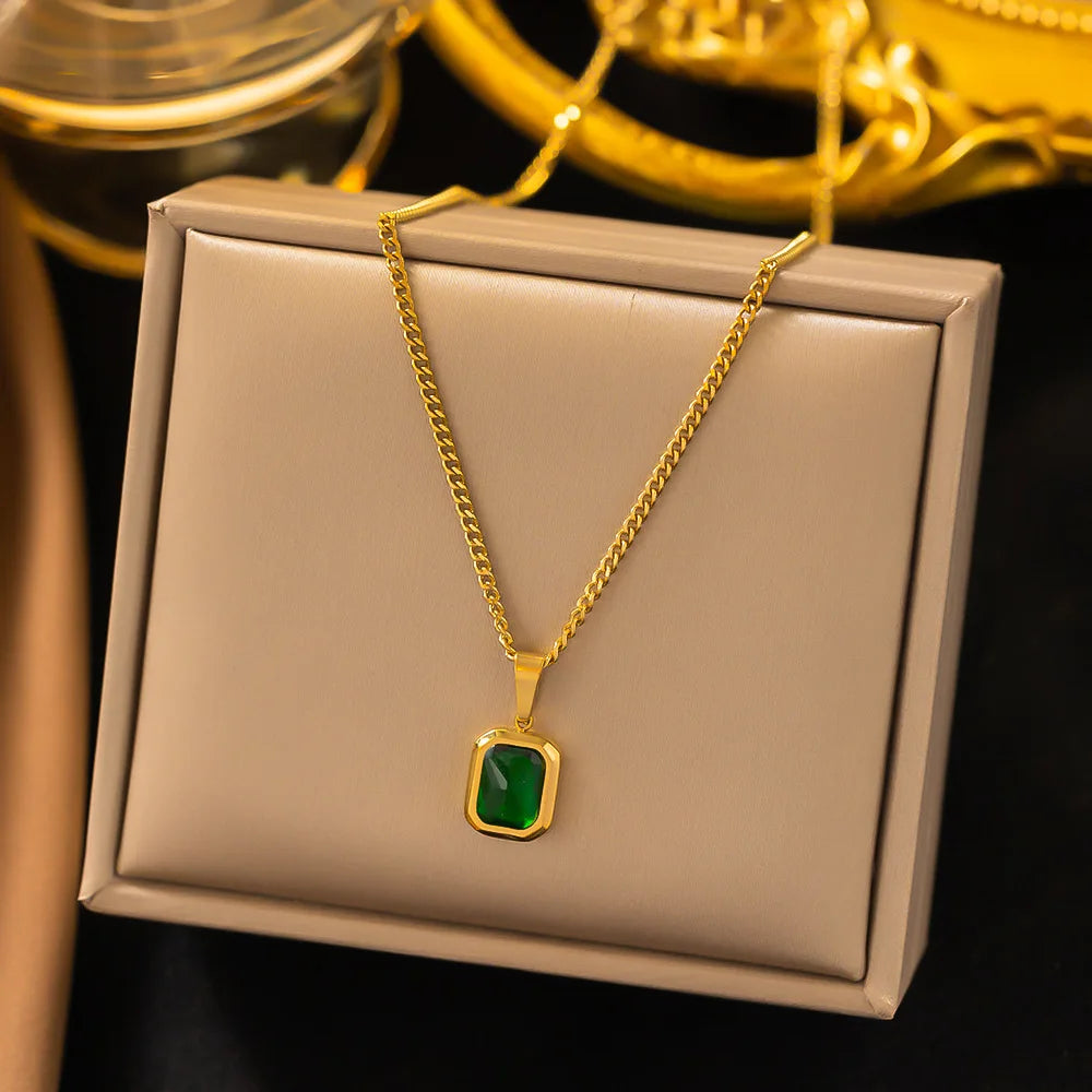 A gold chain necklace with a single square emerald gemstone.