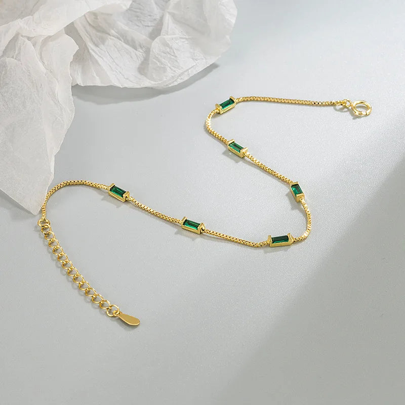 A minimalist gold bracelet with emerald accents.

