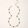 A minimalist gold choker with green and clear gemstones.