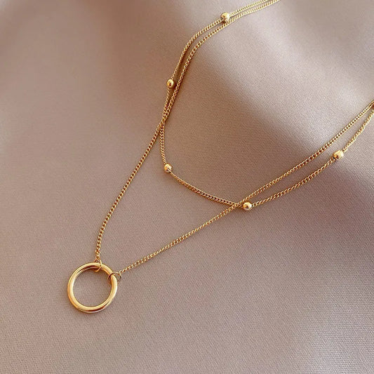 A layered gold necklace with a circle pendant and small beads.