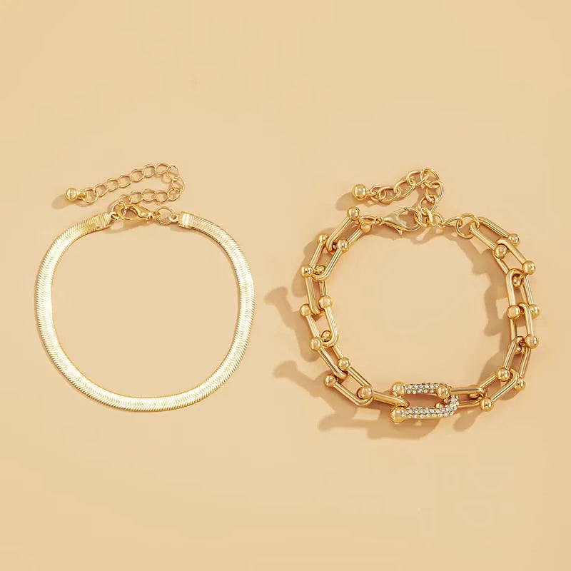 A set of two dainty gold bracelets, one with a chain link design and the other with a flat design.