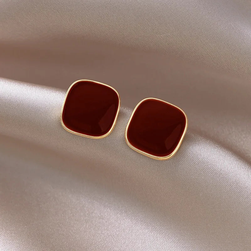 A pair of small red square earrings with a gold frame.