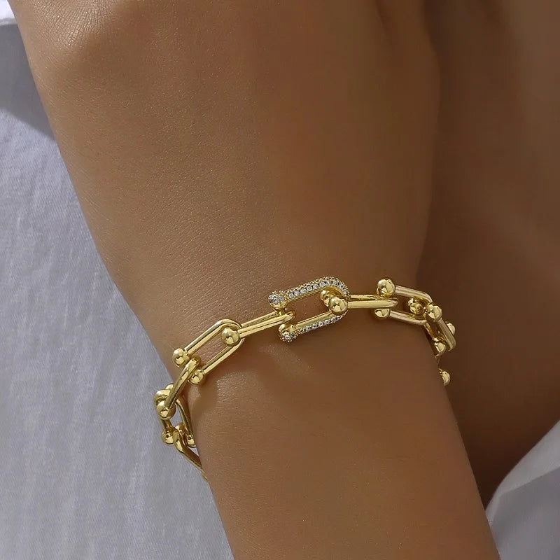 A set of two gold bracelets, one with a chain link design and the other with a flat band.