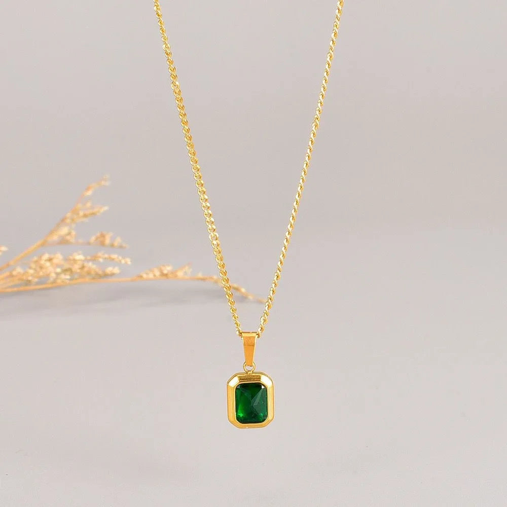 A gold chain necklace with a square emerald pendant.