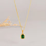 A gold chain necklace with a square emerald pendant.